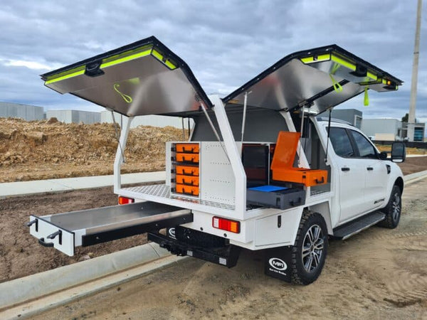 White truck with open cargo bed and additional storage compartments in an outdoor setting.