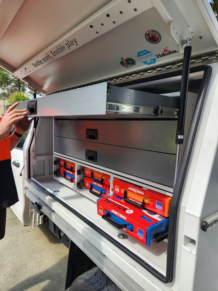 Open tool storage compartment with various tools inside, showing a person's hand reaching in.